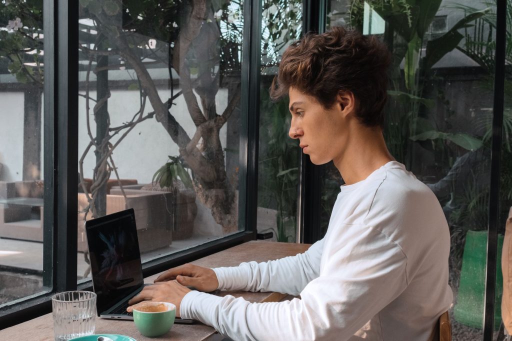 Une personne travaille sur son ordinateur portable dans un café, illustrant un side business mené en parallèle de son emploi